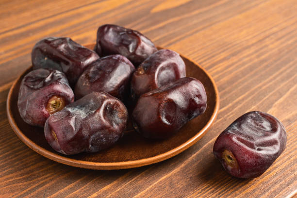Dried organic date fruits in a plate on wooden table.