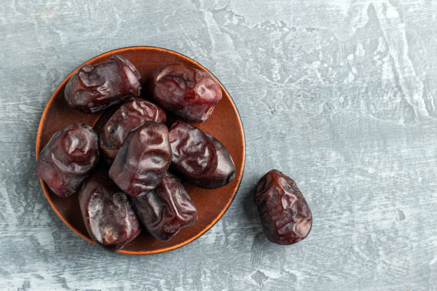 Dried organic date fruits in a plate on a gray background top view.