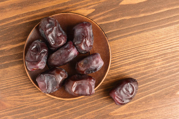 Dried organic date fruits in a plate on wooden table, top view.