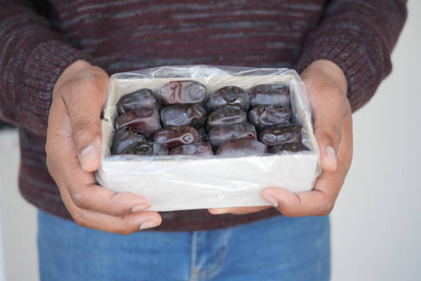 A person holds a clear bag of fresh dates against a contrasting dark background